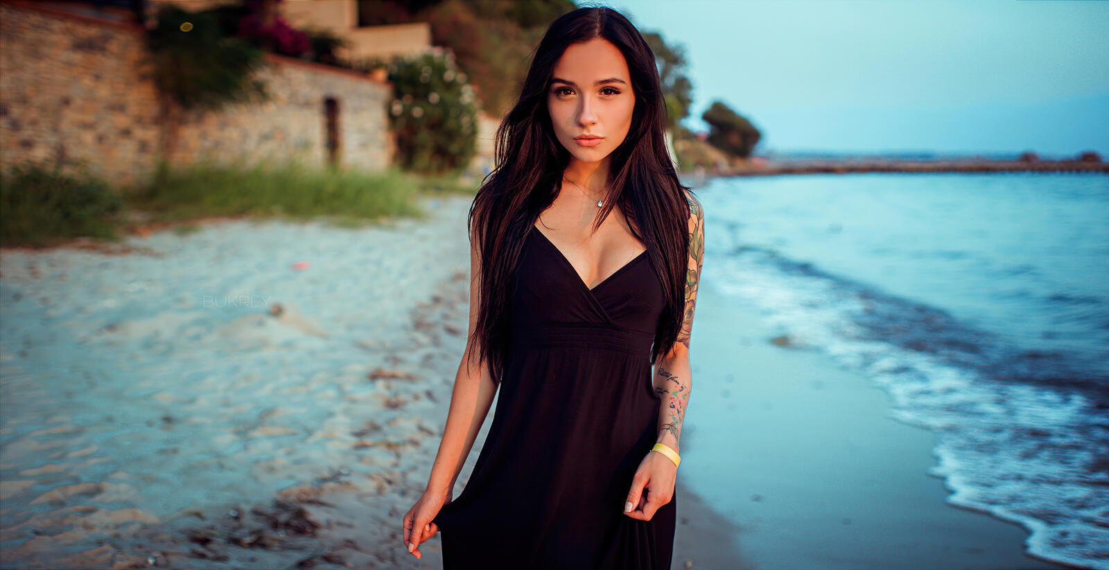 Free photo Charming brunette in a black evening gown walking along the beach