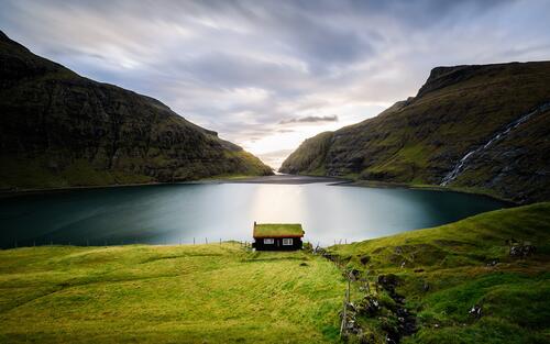 Одинокий домик на берегу озера с зеленой травой на крыше