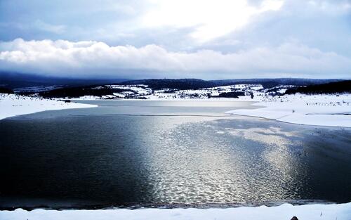 Гладкая поверхность озера со снежными берегами