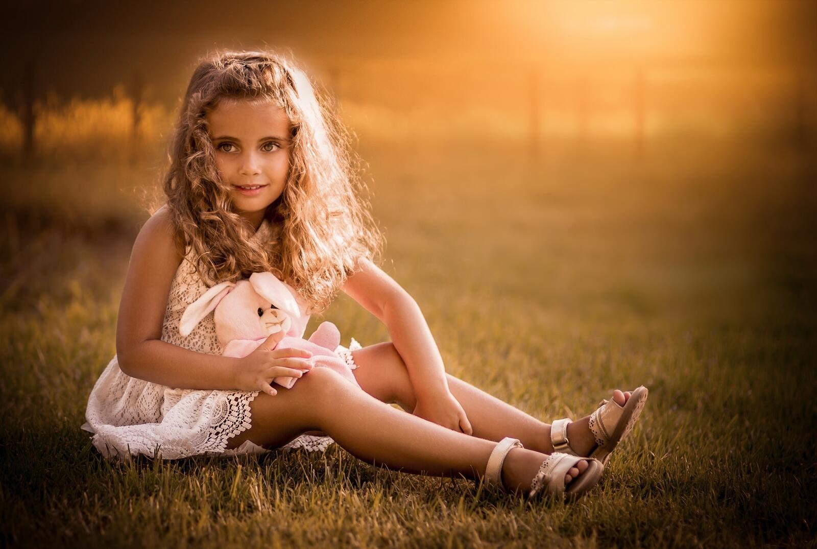 Бесплатное фото Малышка сидит на зеленой лужайке с зайчиком