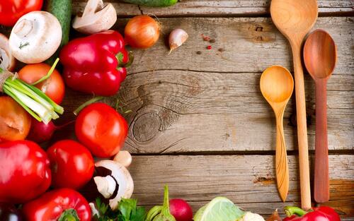 Fresh vegetables with wooden spoons on a wooden background