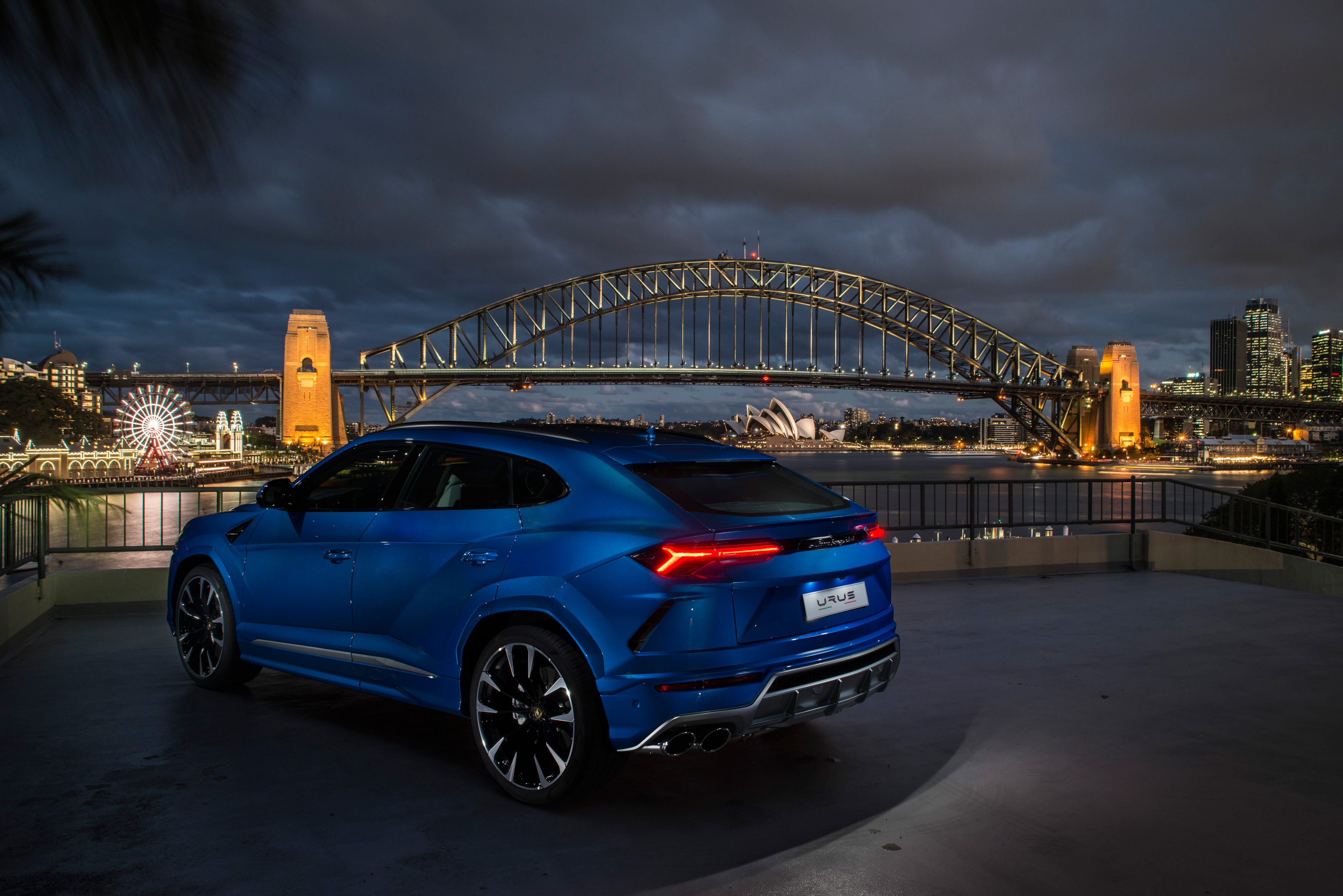 Blue Lamborghini Urus against the backdrop of a large bridge