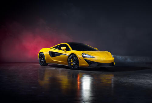 A yellow Mclaren 570S Spider in a black smoky room.