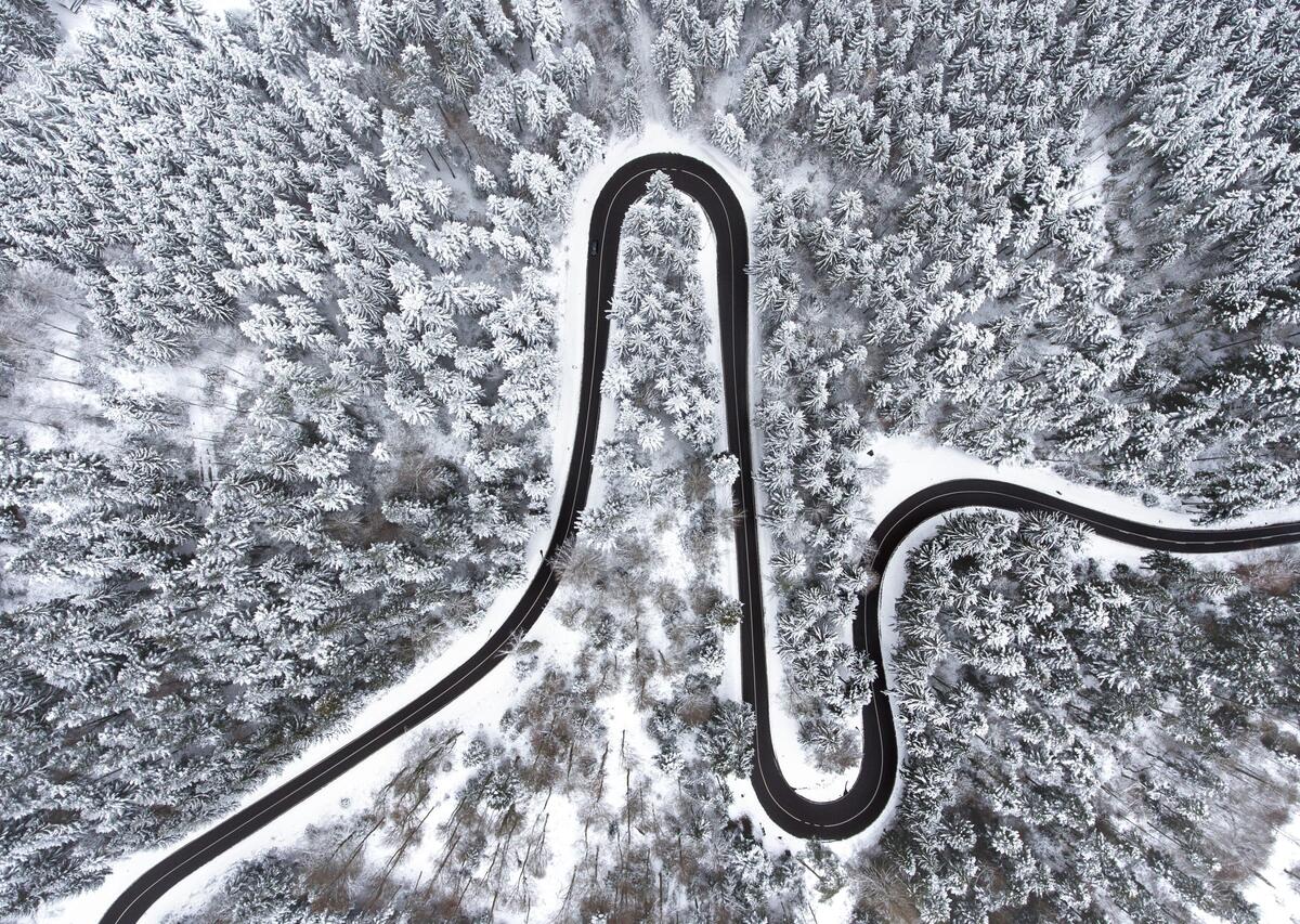 Извилистая автомобильная дорога в снежном лесу вид сверху