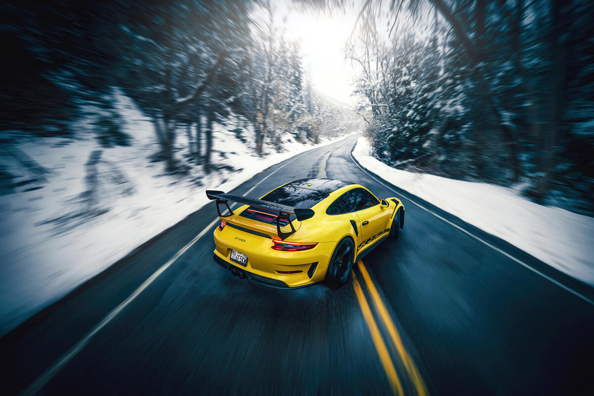 Желтый Porsche GT3 на загородной зимней дороге едет боком