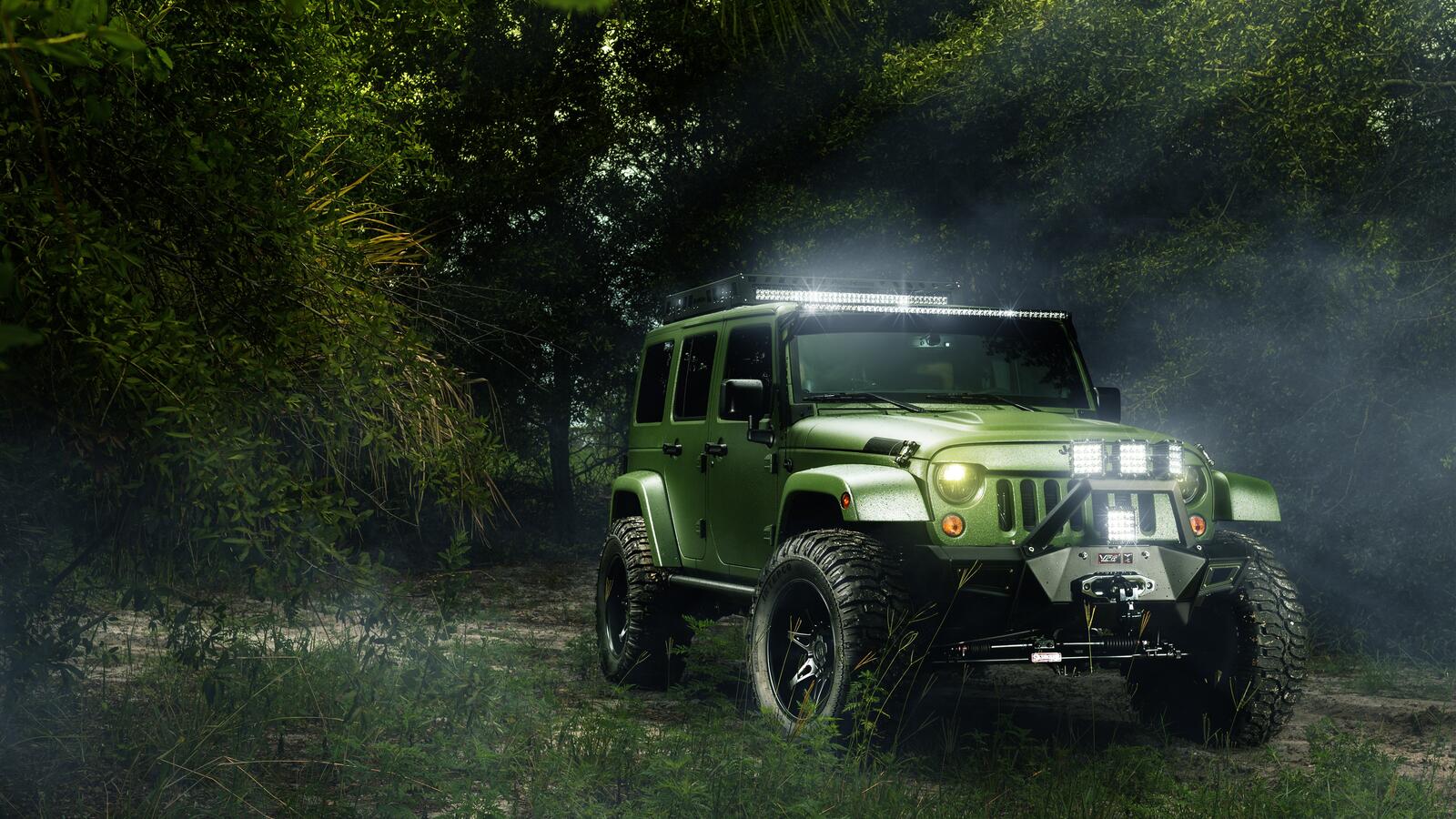 Free photo Green Jeep Wrangler in the woods with lights on