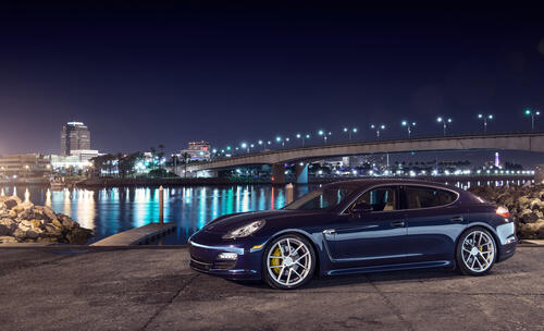 A blue Porsche Panamera against the backdrop of the city at night.