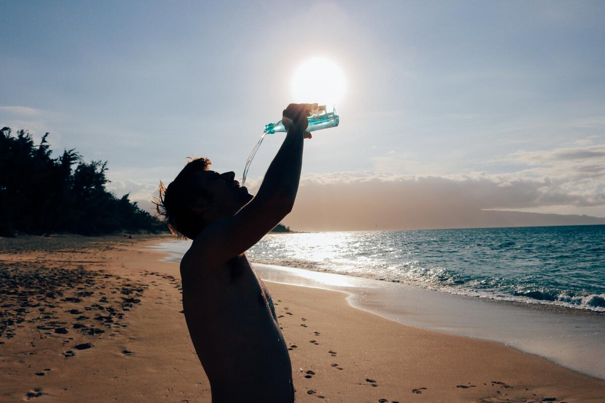 Мужчина пьет воду из бутылки на берегу моря