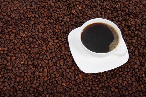 A cup of coffee stands on coffee beans
