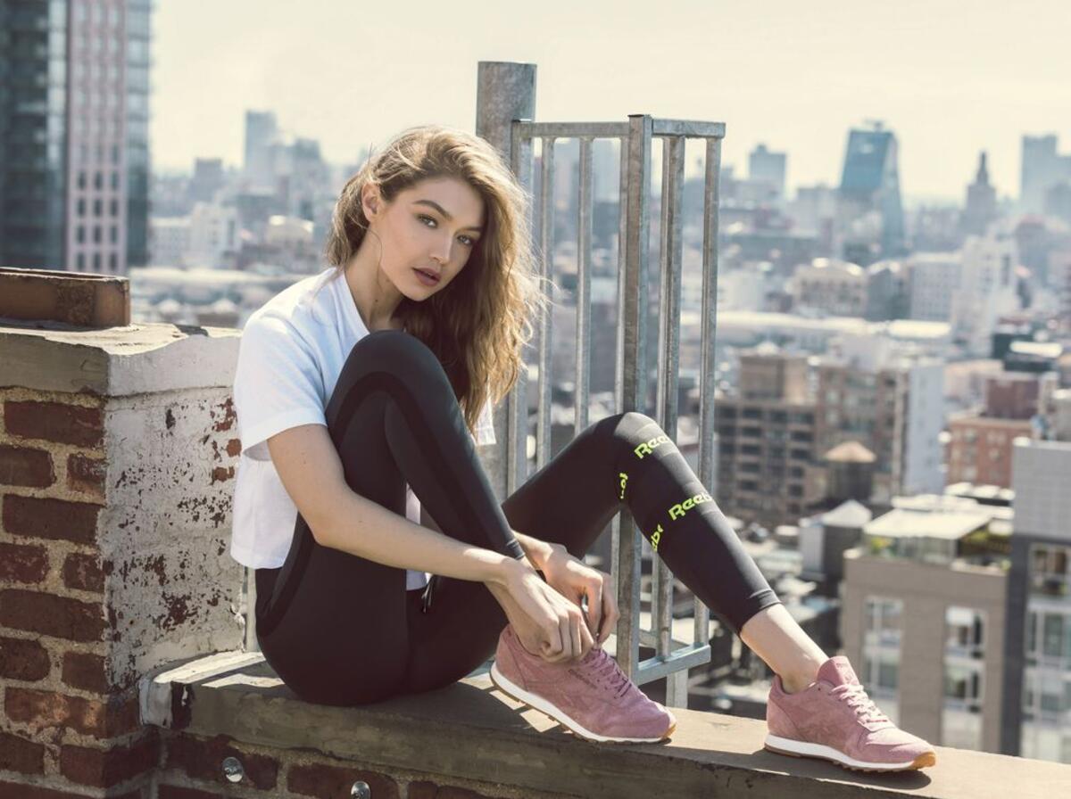 Gigi Hadid in sweatpants sits on the edge of the roof of a building