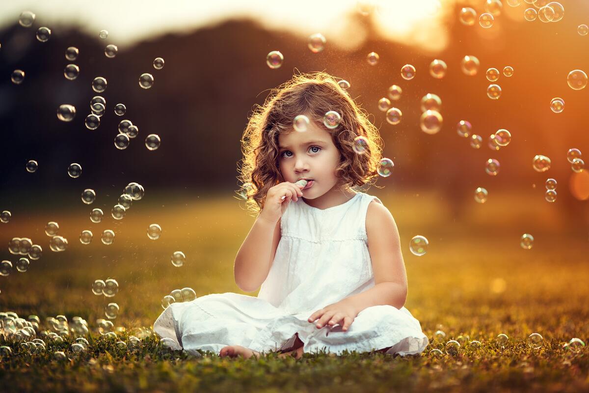 Маленькая девочка в белом платье надувает мыльные пузыри