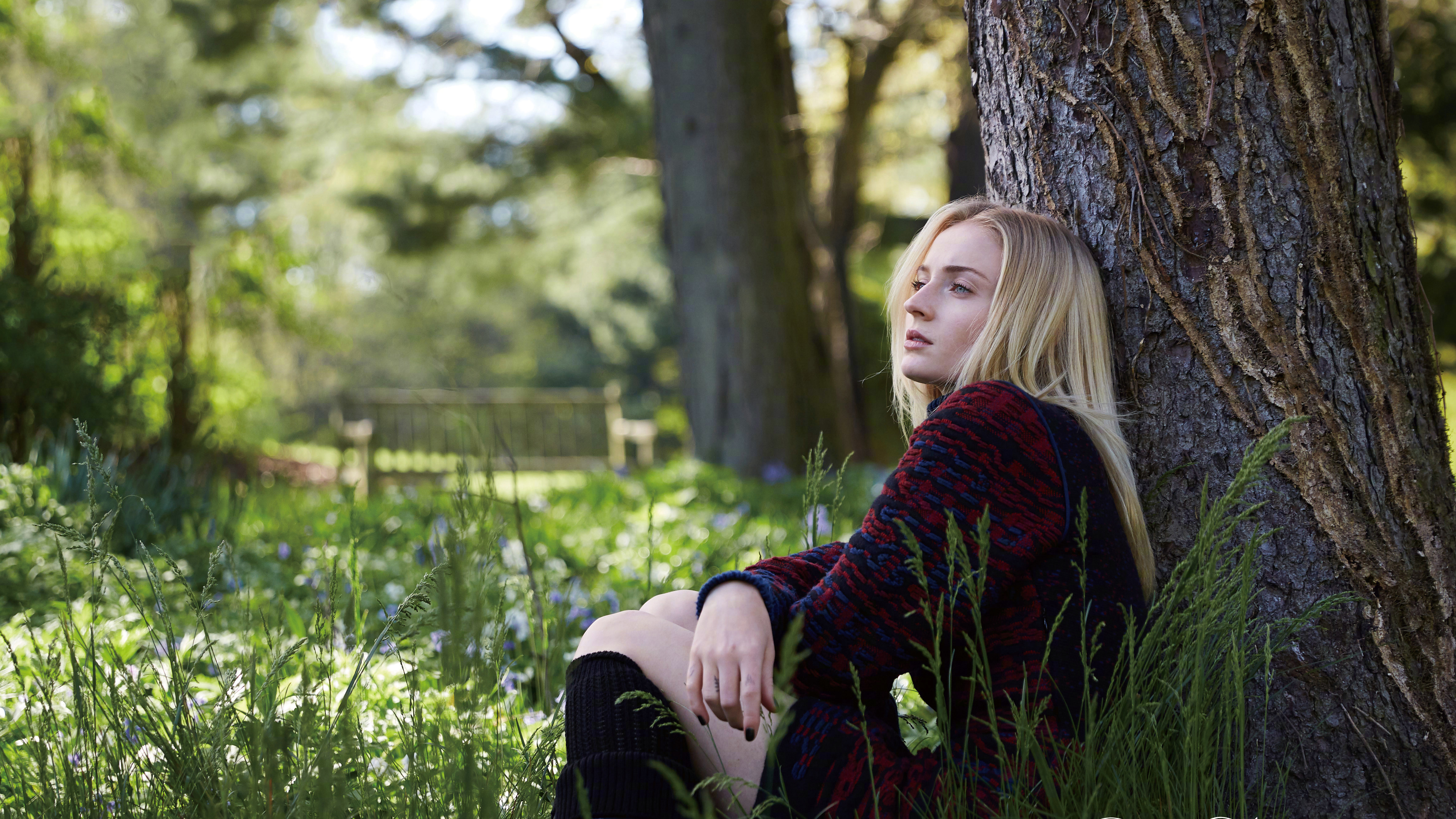 Sophie Turner sits by a tree