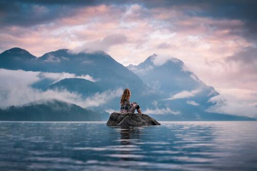 Девушка сидит на камне среди озера