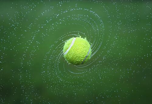 Мокрый теннисный мячик кружится в воздухе