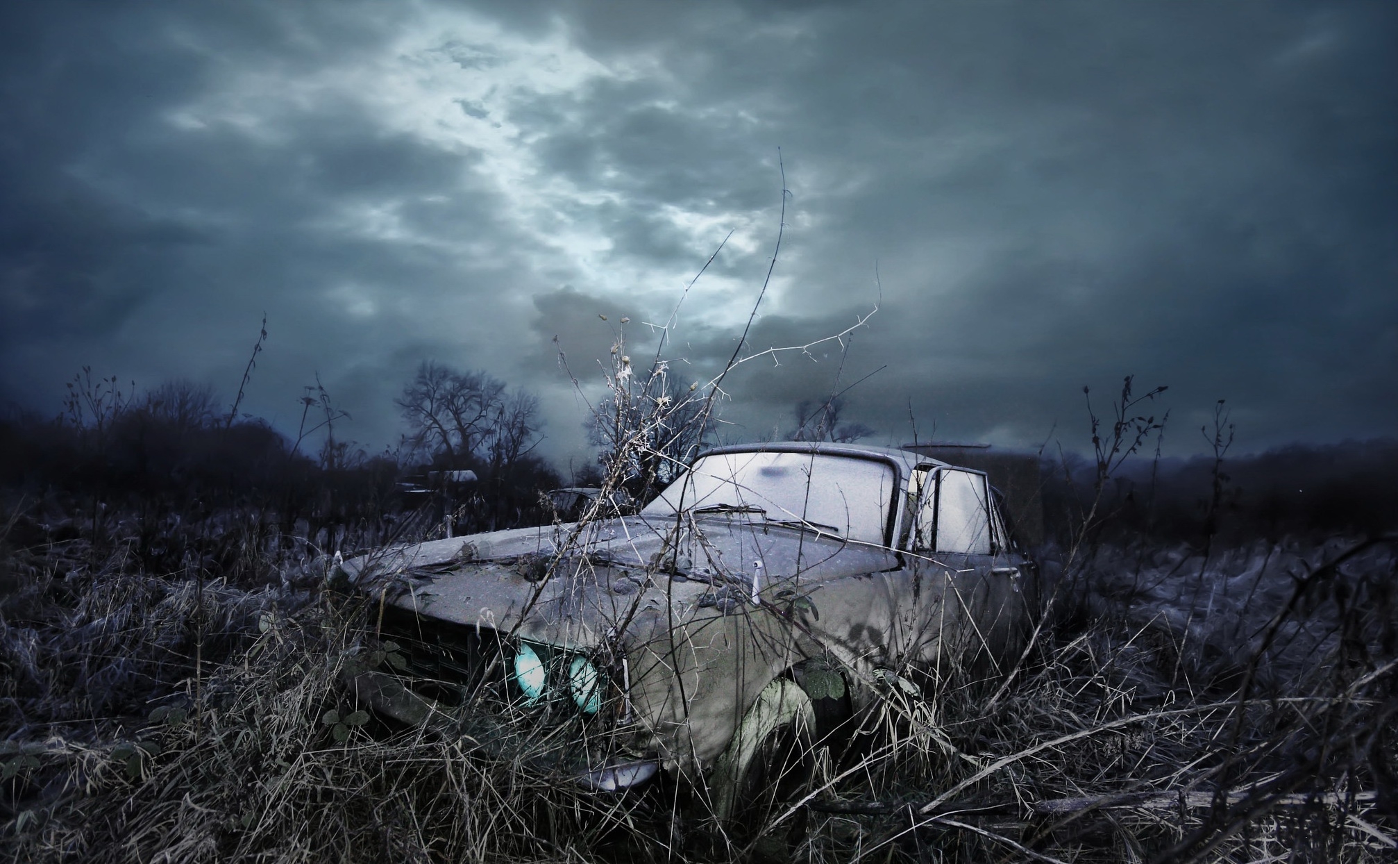 An abandoned car stands in a field in bad weather