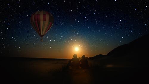 Молодая пара в ночи под звездами и наблюдает пролетающий воздушный шар