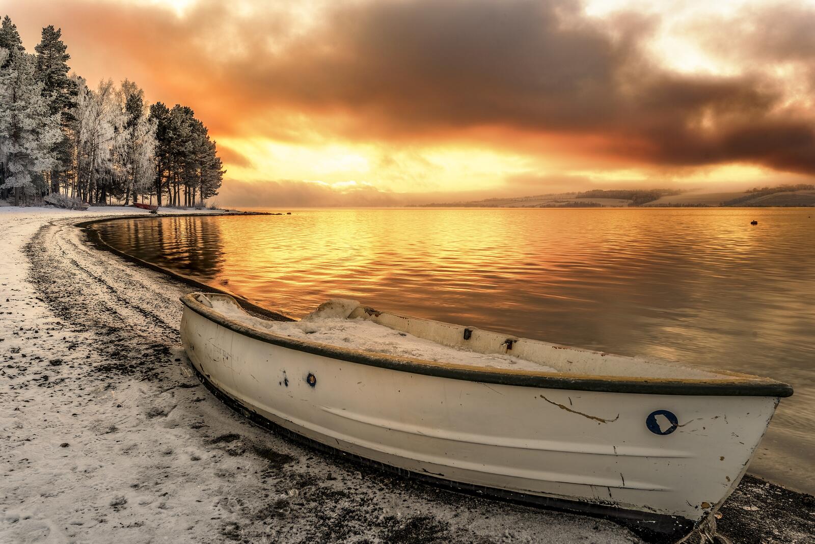 Free photo A boat on the shore of a lake with snow banks