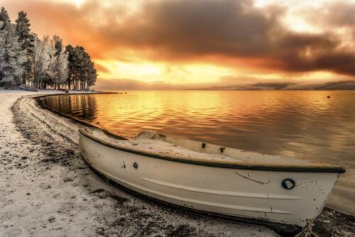 A boat on the shore of a lake with snow banks