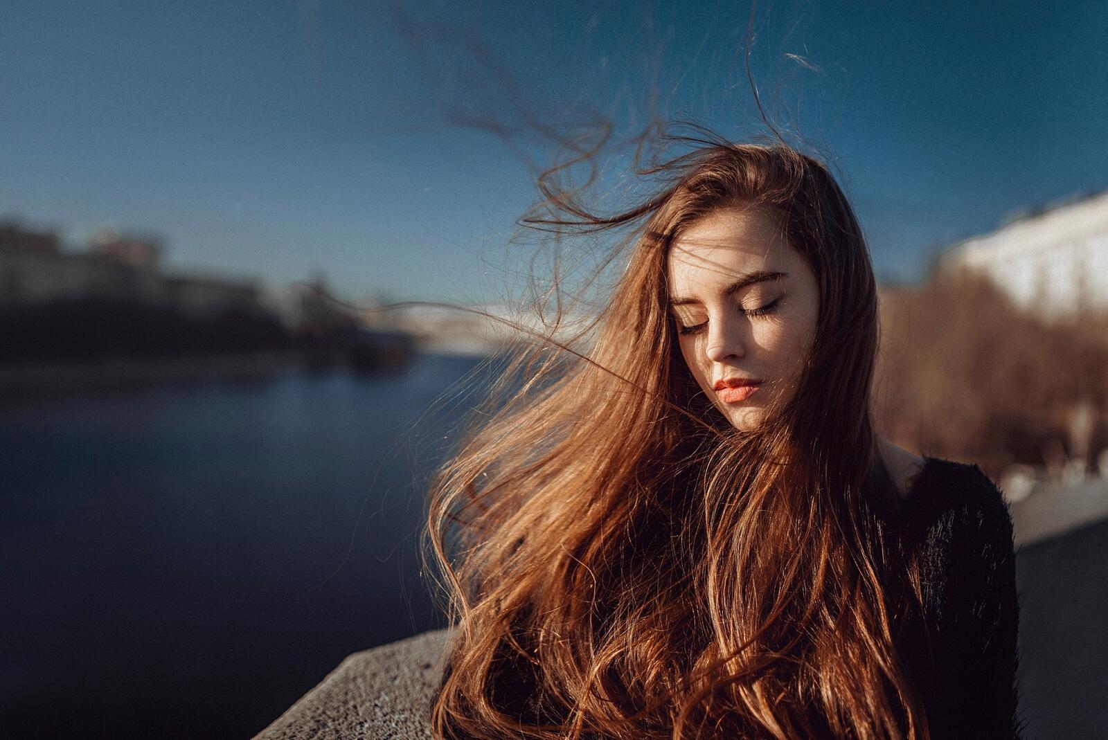 Бесплатное фото Темноволосая девушка стоит на ветру с закрытыми глазами