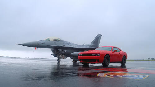 Red Dodge Challenger next to a military fighter jet.