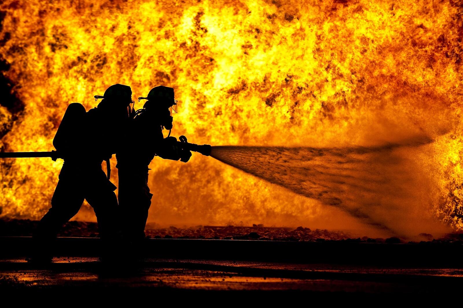 Free photo Silhouette of firefighters against the backdrop of a large fire