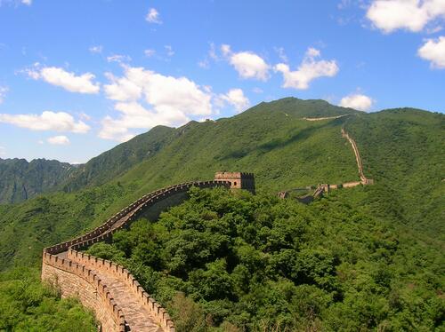 The Chinese wall runs through rolling hills with green trees