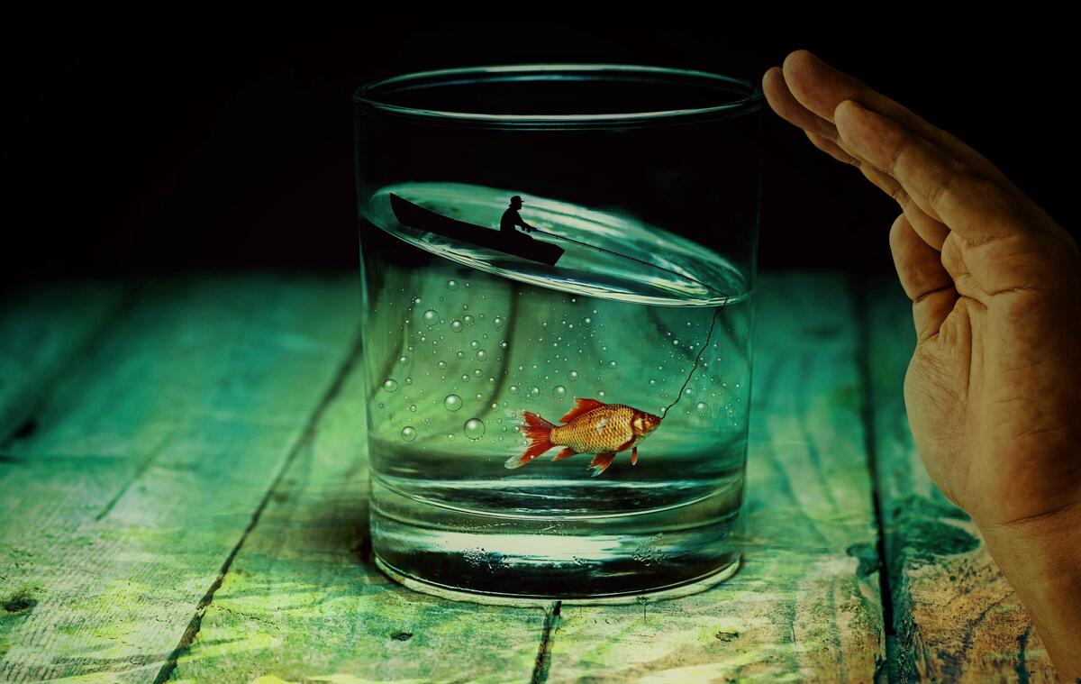 A fisherman on a boat in a clear glass of water caught a goldfish
